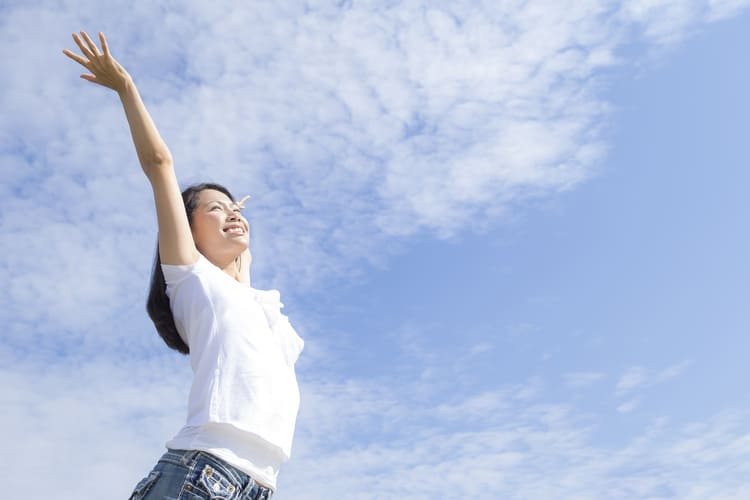 青空の下で両手を広げる女性